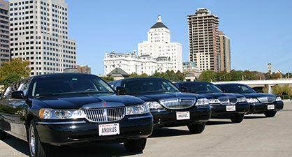 A row of black luxury limousines parked in front of tall buildings on a sunny day.