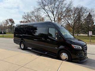 Black van parked on a street with trees and cloudy sky in the background.