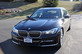 Black BMW sedan parked on the street with a personalized license plate and trees in the background.