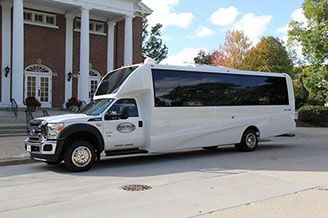 White shuttle bus parked in front of a brick building with columns.