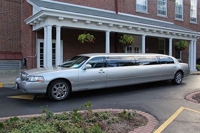 White stretch limousine parked in front of a brick building with white columns and hanging flower baskets.