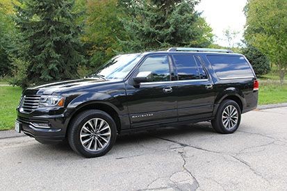 Black SUV parked on a street with trees and greenery in the background.